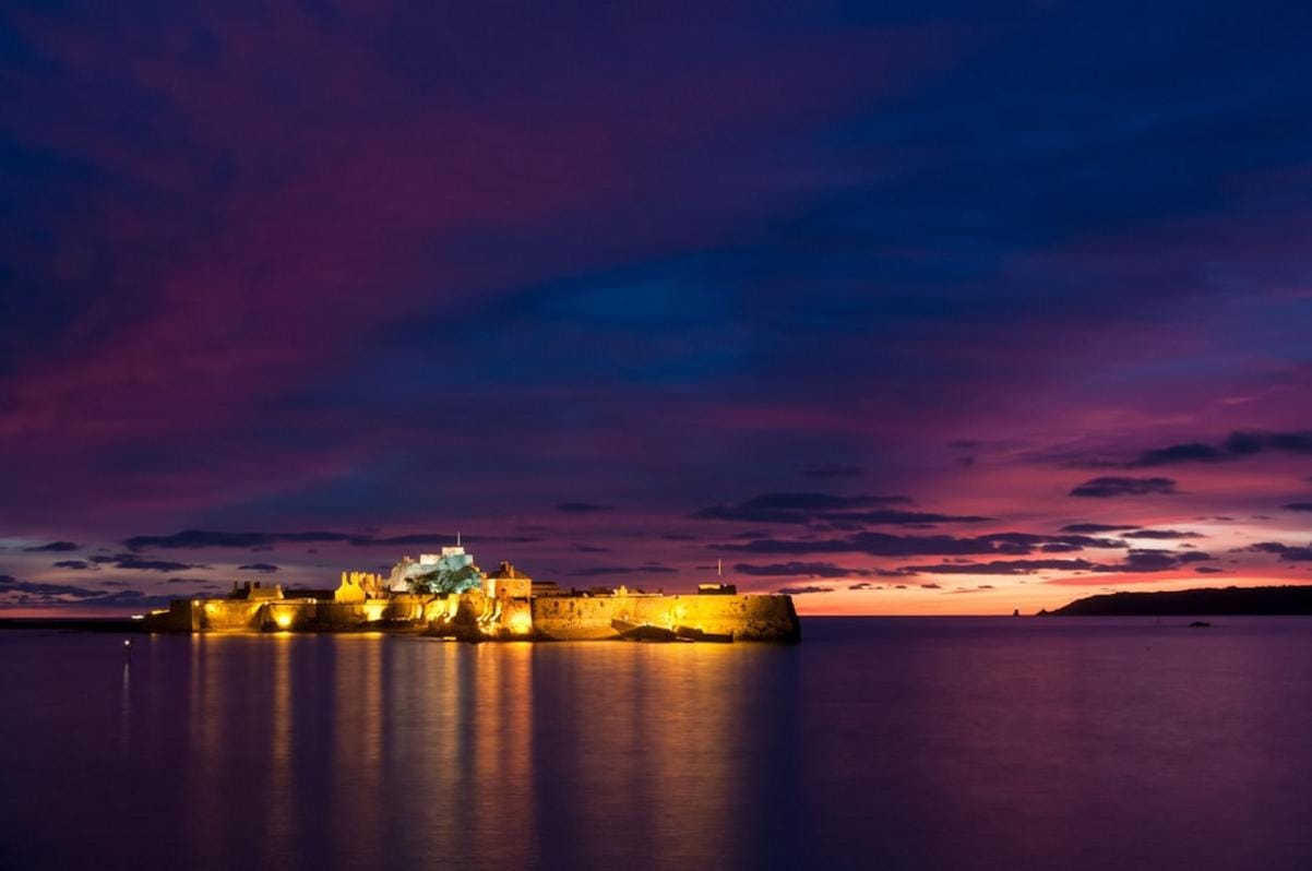 A view of Bodrum Castle illuminated at sunset with yachts in the marina, showcasing its historic grandeur and harbor life