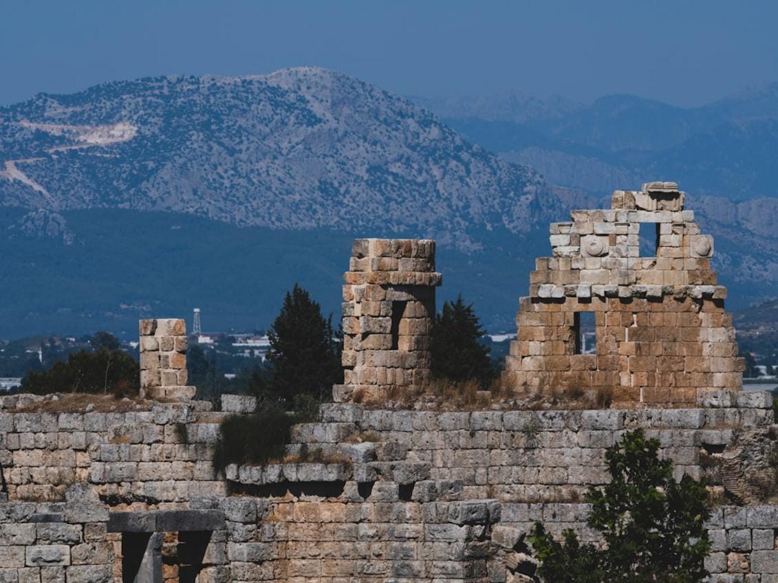 A panoramic view of the ancient ruins of Perge with lush green surroundings and mountain backdrop, illustrating Turkey's rich history