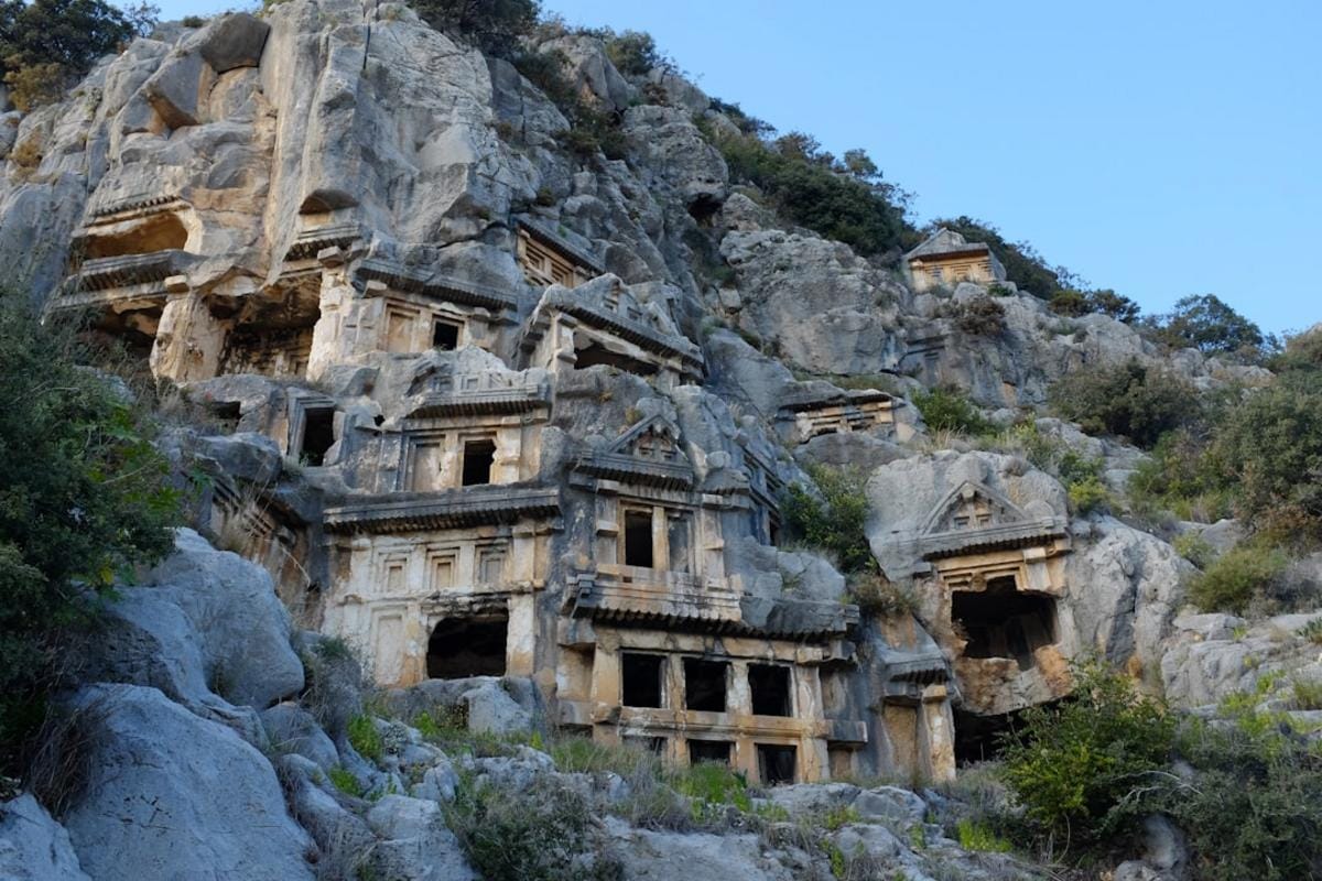 Ancient Lycian tombs overlooking the sea in Kaş with boats sailing nearby
